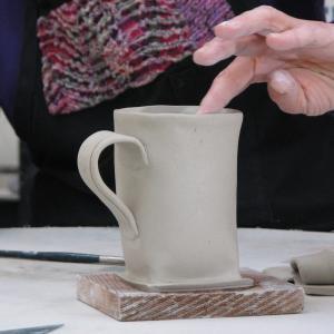 A finger gently sweeps along the inside of an unfired clay coffee cup.