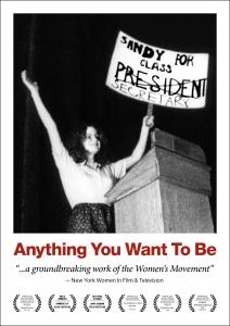 In this black and white still from the film, a young woman triumphantly holds up a sign that reads “Sandy For Class President.” The word ‘President’ is crossed out and underneath is written “Secretary”. She’s onstage at a lectern. Film title "Anything You Want To Be" and festival award laurels.