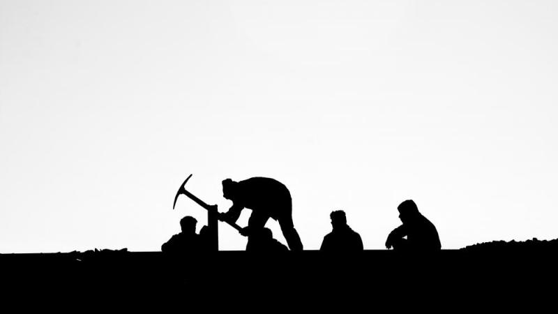 Black and white photo of five people silhouetted, with one holding a pick axe.