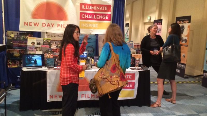 Two New Day Films filmmakers converse with conference attendees at the booth.