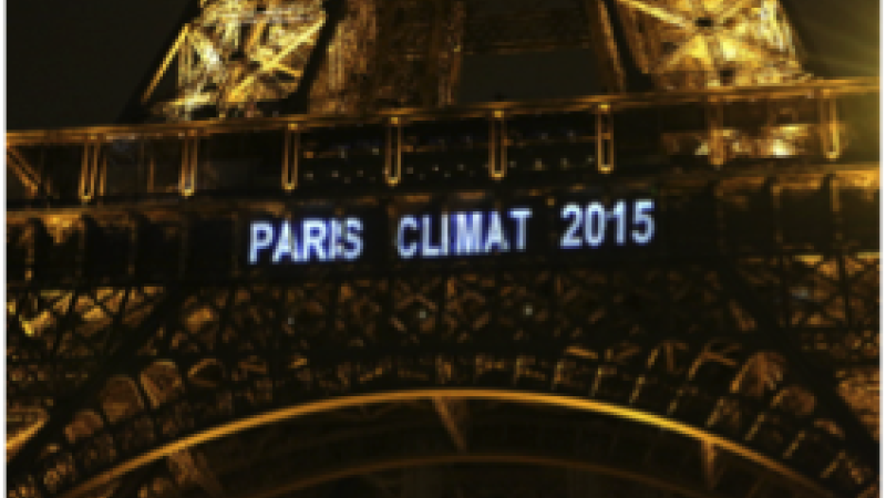 A close up image of the Eiffel tower at night with the words “Paris Climat 2015” projected in white letters on it.