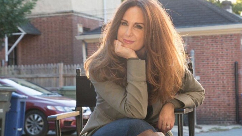 Director Andrea Kalin sits in a director's chair with her hand on her chin, and looks directly at the camera.