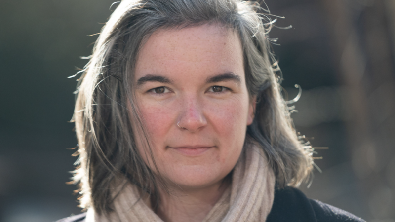 Headshot of woman with fair skin and gray medium length hair wearing a beige scarf