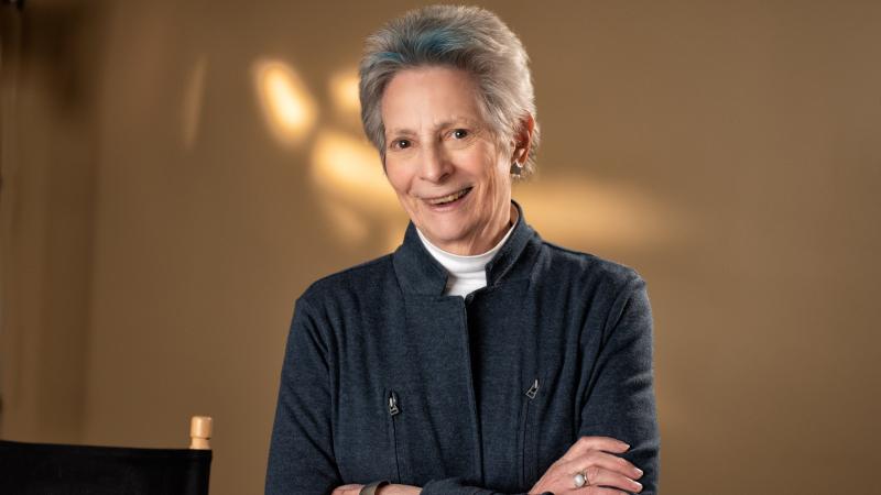 A woman with short, grey hair looks at the camera and smiles.