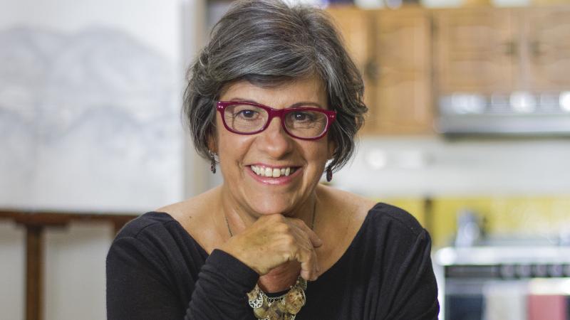 Photo of filmmaker Luisa de la Ville staring into the camera and smiling. They have short, greying hair and red glasses.