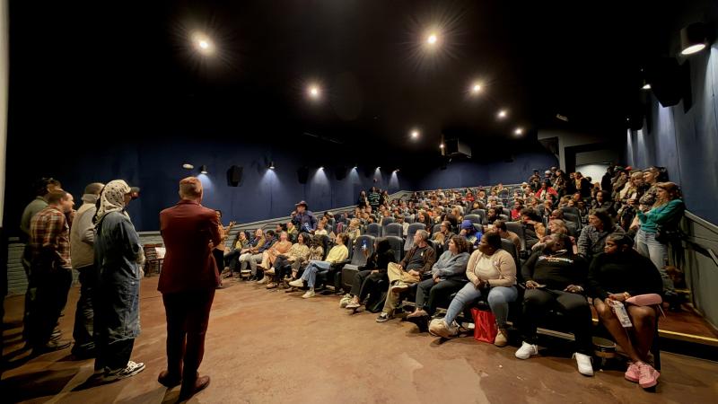 Five people stand at the front of a small theater speaking on a panel after a New Day Films screening. People of a range of ethnicities and genders fill nearly all of the seats, and more line the walls.