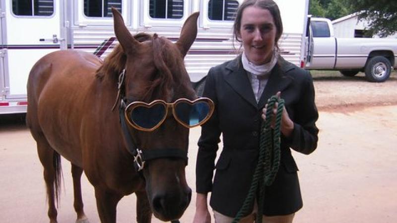 Woman standing next to a horse with huge sunglasses on.