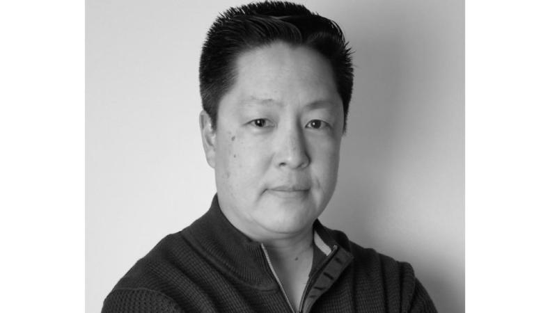 New Day Director Jon Osaki, a Japanese American, stares directly into the camera in this black and white headshot.