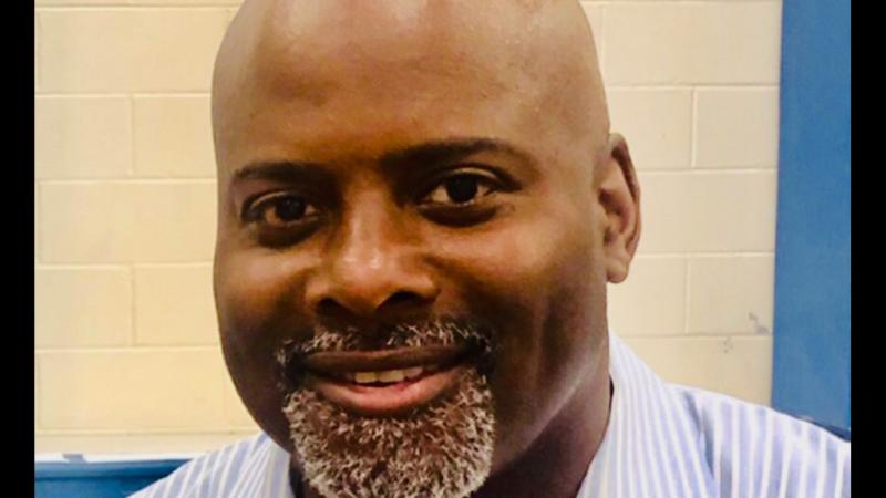 A headshot of New Day Filmmaker Mike Mascoll, a bald African-American man with a grey goatee. He looks directly at the camera and smiles.