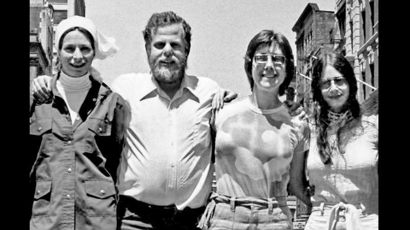 In this black and white shot from the 1970s, New Day Co-founders link arms and smile at the camera. From left to right:  Liane Brandon, Jim Klein, Julia Reichert, and Amalie R. Rothschild.