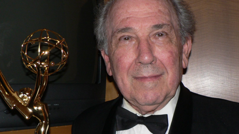 Filmmaker Robert Richter looks at the camera with a slight smile. He is dressed in a black tux. A gold Emmy statue is to his left.