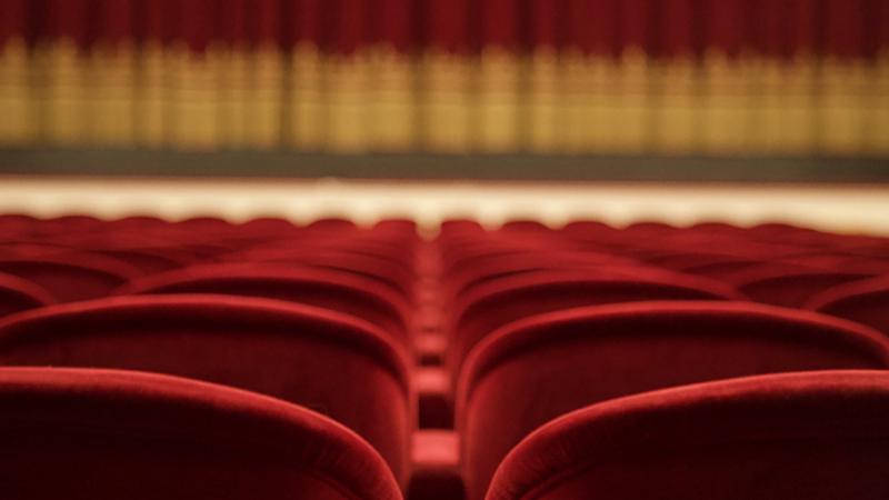 In this empty theater, we see rows of velvet chairs and an out-of-focus stage.