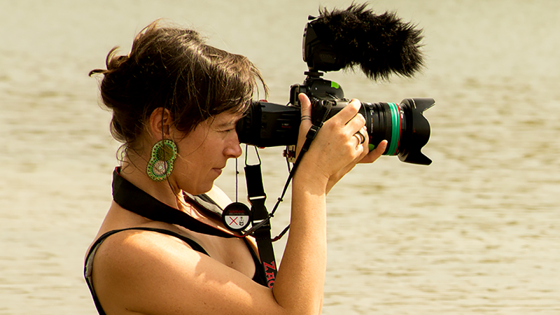 Side view shot of New Day Filmmaker Willow O’Feral, a white woman in her 30s, with dark hair and large earrings, who is looking into a camera.