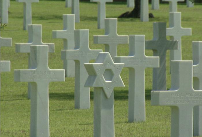 A cemetery filled with tall white stone crosses, a lone headstone with a Star of David in place of a cross.