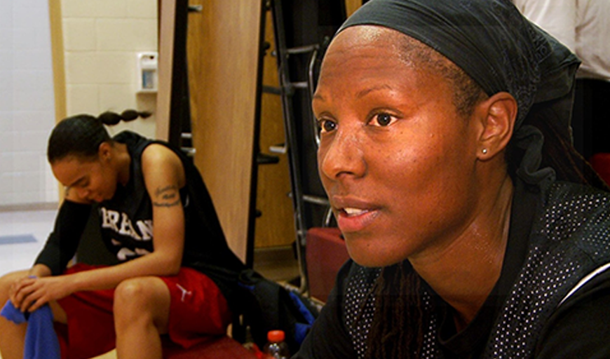 Chamique Holdsclaw, an African-American female basketball star looks intently off camera. Behind her, a teammate sits on a bench and peers at the ground.