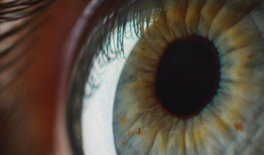 An extreme close up of a human eyeball with dark black pupil. Eyelashes are reflected on the white of the eye.
