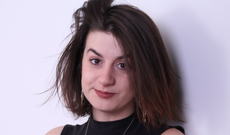 In this headshot, New Day Films director Jillian Karole looks at the camera with a wry smile. She has long, shoulder length hair and brown eyes.