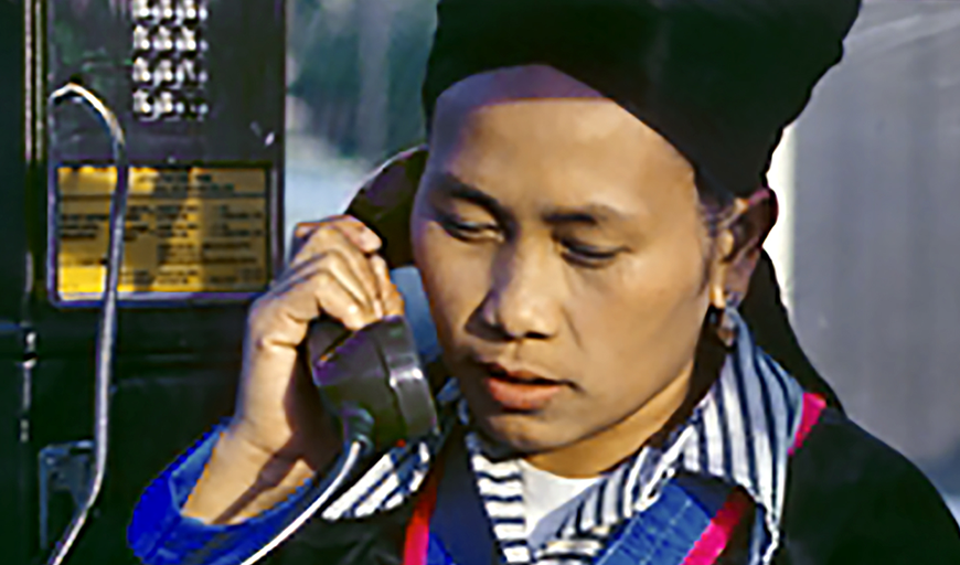 A Hmong man from Laos speaks into a payphone in the United States. His eyes are downcast.