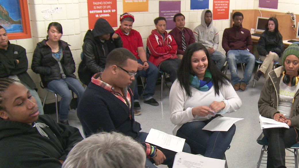 A multiracial group of people sit and talk in a restorative justice circle.