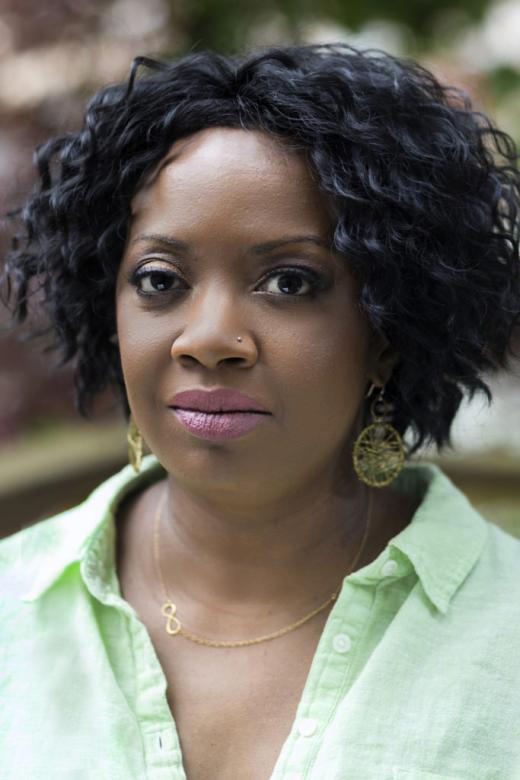 A headshot of New Day Filmmaker Faith Pennick, an African-American woman with wavy shoulder length hair and a pierced nose. She looks directly at the camera with a neutral expression.