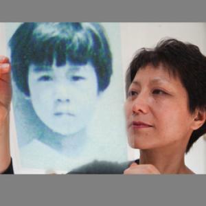 Filmmaker Deann Borshay Liem holds up a black and white photo of a young Korean girl.