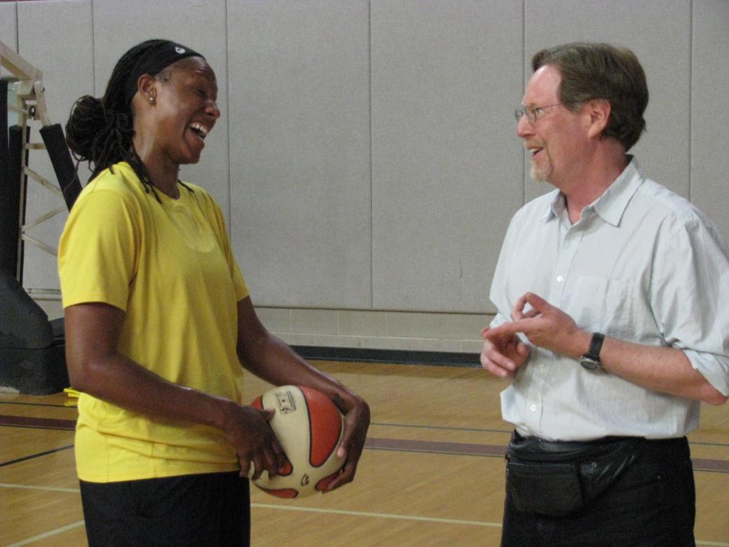 An African-American female, Chamique Holdsclaw, holds a basketball and smiles widely. She is facing a white, middle aged man with dark hair and a goatee, filmmaker Rick Goldsmith, who smiles back at her.