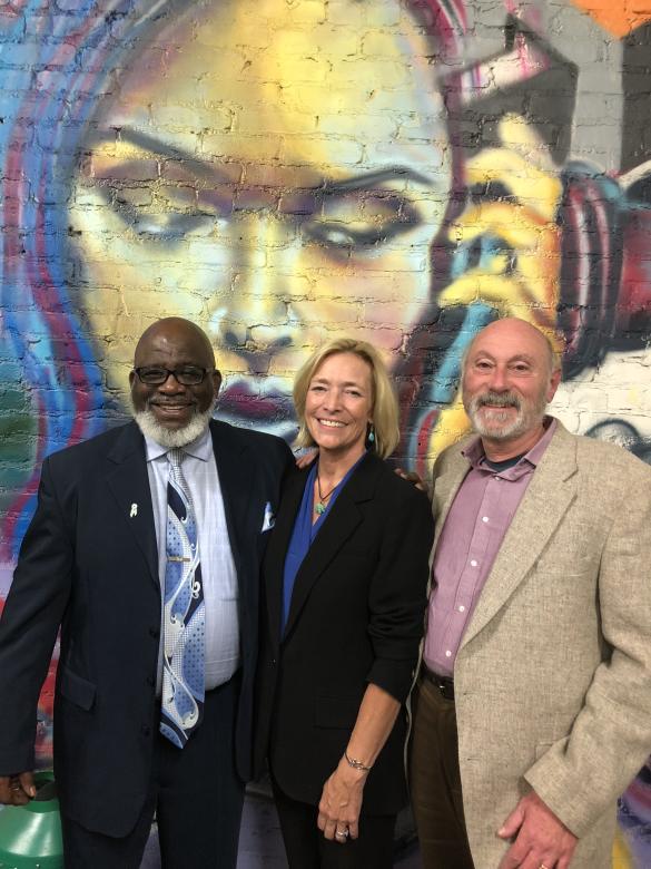Filmmakers Maggie Stogner and Rick Stack pose with Jerry Givens in front of a mural of a Black woman.