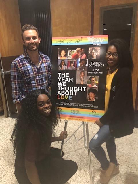 Three young people from the film gather aruond a poster for The Year We Thought About Love and smile for the camera.