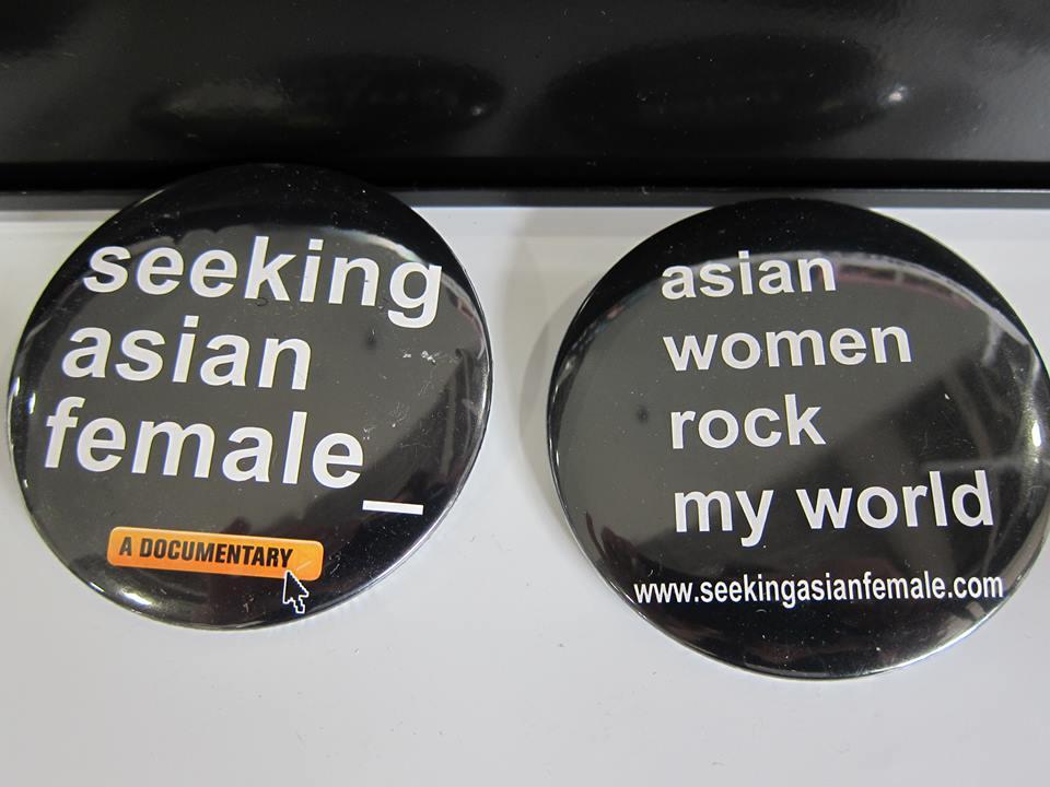 Two black buttons side by side. The button on the left reads “seeking asian female_” in large white letters with the words “A documentary” in all black capital letters on a small orange rectangle. A computer arrow hovers over the orange box. The button on the right reads “asian women rock my world” in large white letters. Beneath this text is a url in smaller white letters that reads “www.SeekingAsianFemale.com”.