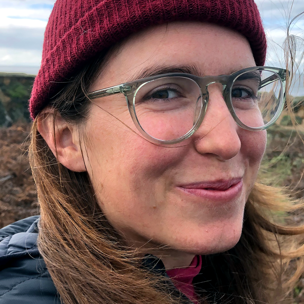 A close-up shot of Amy's face, she's wearing a red beanie and her light brown long hair is blowing in the wind.