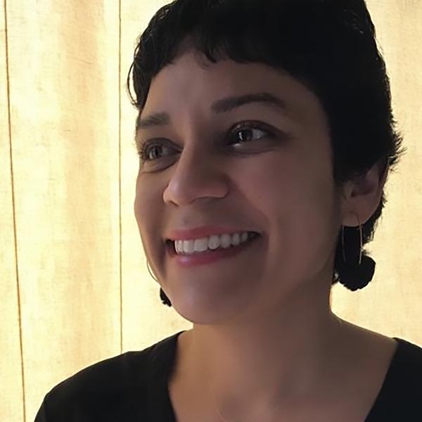 Michelle Plascencia smiles slightly off to her right, backlit in front of a yellow wall.