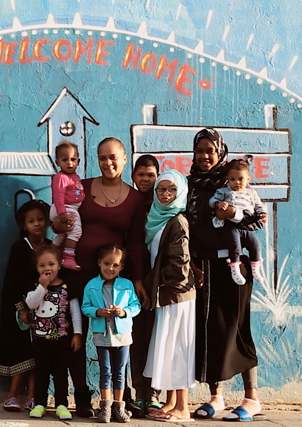 photo with women and children standing in front of mural that reads welcome home
