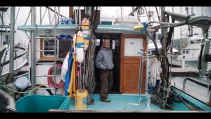 Dick Ogg is standing on the deck of his boat outside the wheelroom, smiling 