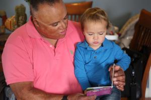 Hispanic man with visible scars wearing a polo shirt reading to a young child in his lap