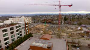 A wide, aerial shot of a red construction crane towering over a hole the size of a city block in an otherwise residential neighborhood.