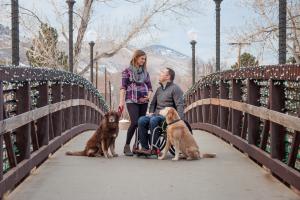 Woman standing looking down at man in wheelchair with two dogs, all of them on a walking bridge.