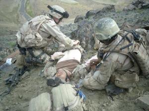 Soldier lying on the ground with his shirt off being cared for by Army medics.