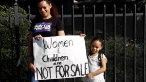 Mother and daughter hold up a sign that says "Women and Children are Not for Sale"