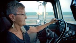 A woman is driving a truck. Her face is in profile and she is holding a steering wheel.
