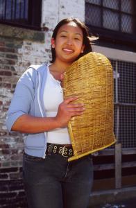 Young woman holds Cambodian basket in front of brick wall