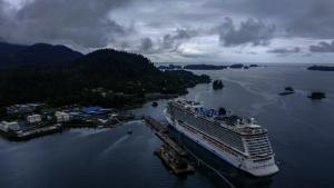 An aerial photo of the Sitka harbor shows a cruise ship parked at the dock, looming over the small town.