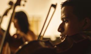 close up (profile) of Edixon playing viola, in the background another young musician 