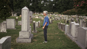 Woman standing in cemetery next to tombstone with Chinese characters