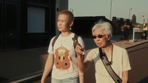 A young person walks alongside their elder who is pointing into the sunlight ahead