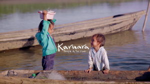 An Indigenous boy and girl in river, girl holding bucket of fish on head