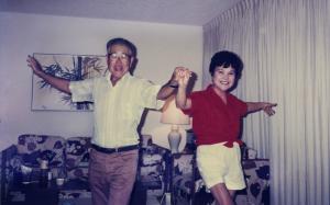 A middle-aged Japanese-American couple hold hands and dance in their living room. Their faces are lit with smiles as they face the camera, arms extended.