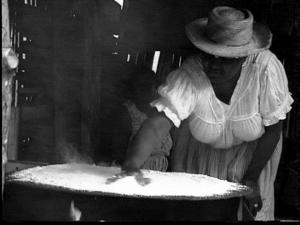 A woman is standing over a "comal" baking a disk of cassava bread