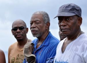 Three Garifuna men standing in a row looking out. 