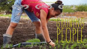 A young Hawaiian woman in shorts and a sleeveless shirt in a field, bending over, planting tiny vegetable starts. Her long brown hair is braided and hangs over her head, almost touching the ground. It is a bright sunny day. Title, "Growing People" and a row of film festival award laurels.