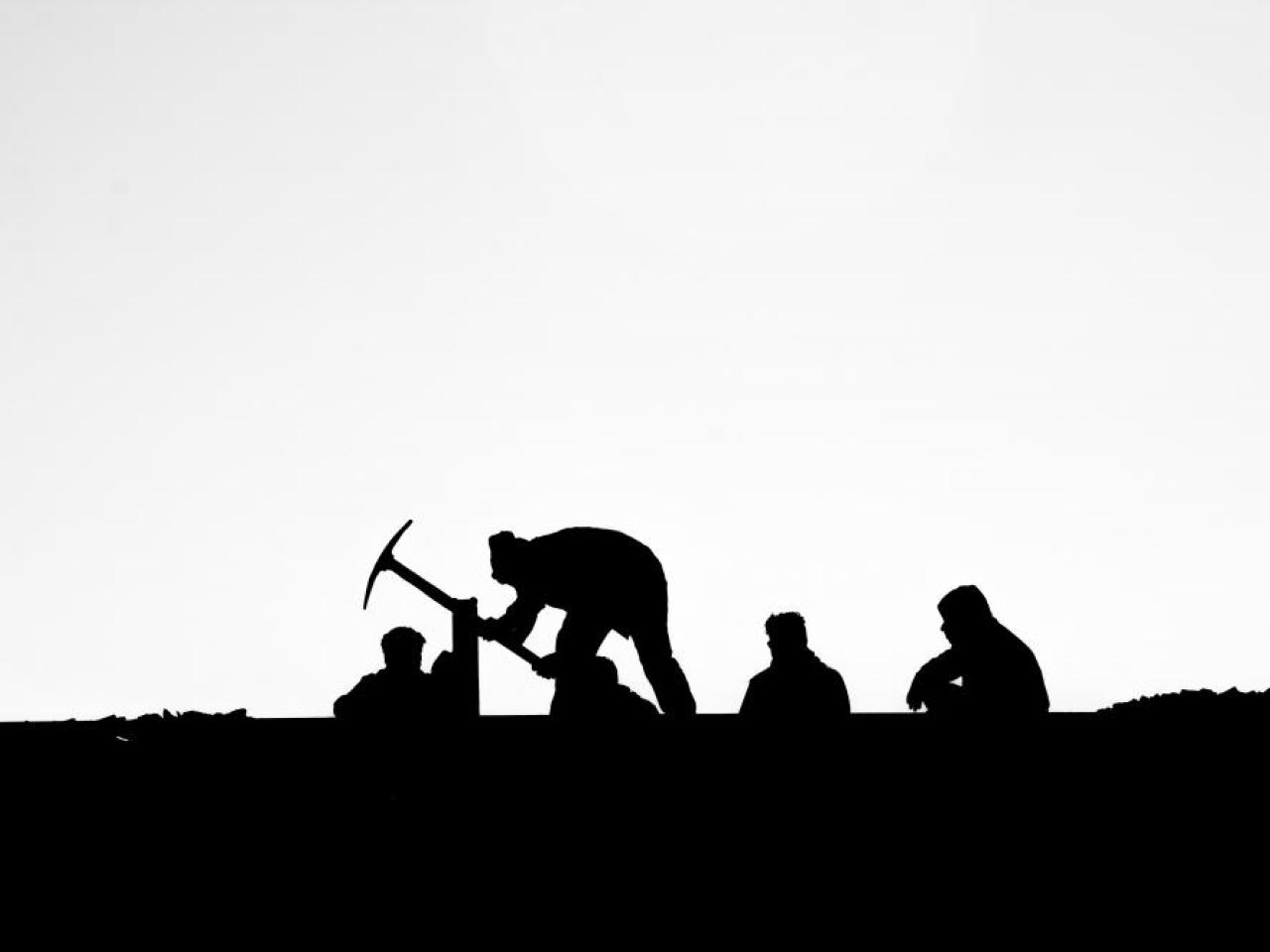 Black and white photo of five people silhouetted, with one holding a pick axe.